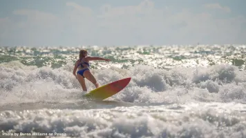 A woman rides the waves on a surfboard during a sunny day at the beach, capturing the essence of summer.