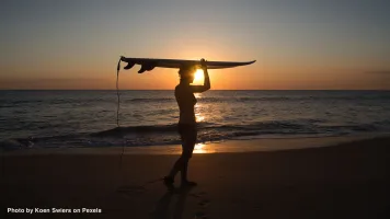 Silhouette of a surfer carrying a board at sunset on Melbourne Beach, Florida.