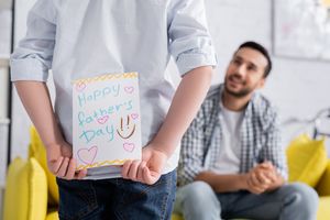 child holding a handmade Father's Day card in front of their dad